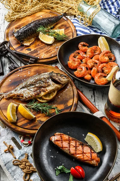 Seafood, grilled dorado fish, grilled salmon steak, smoked mackerel fish and fried shrimps with lemon and rosemary on wooden background with map and fishnet. Healthy food, top view