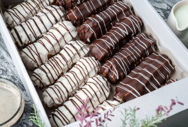 Kutuda beyaz ve çikolata jöleli ekler ya da profiteroller ve gri ahşap arka planda bahar çiçekleriyle kaplı tabağın üzerinde. Tatlılar, tatlı ve pasta, üst manzara, kapat.