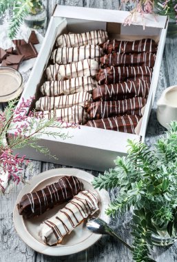 Kutuda beyaz ve çikolata jöleli ekler ya da profiteroller ve gri ahşap arka planda bahar çiçekleriyle kaplı tabağın üzerinde. Tatlılar, tatlı ve pasta, üst manzara