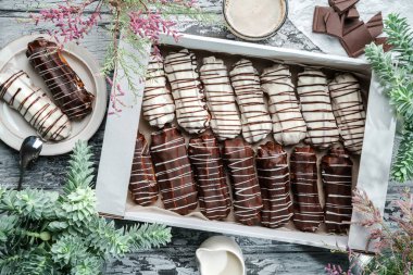 Kutuda beyaz ve çikolata jöleli ekler ya da profiteroller ve gri ahşap arka planda bahar çiçekleriyle kaplı tabağın üzerinde. Tatlılar, tatlı ve pasta, üst manzara