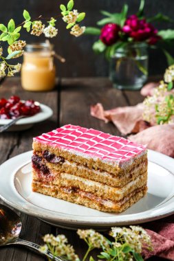 Koyu ahşap arka planda çilek ve çiçeklerle kaplı, vişneli ve yoğunlaştırılmış sütle bir parça lezzetli bisküvi keki. Tatlılar, tatlı ve pasta, ev yapımı kekler, yakın plan, seçici odaklanma