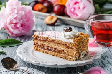 Taze erik ve şakayık çiçekleri ile gri zemin üzerinde krema ve erik reçelli lezzetli kek parçası. Tatlılar, tatlı ve pasta, yakın çekim, seçici odaklanma