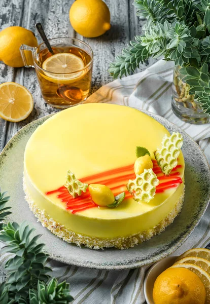 Yellow mousse cake with mirror glaze, limons on light wooden background with cup of tea and plants. Sweets, dessert and pastry, top view