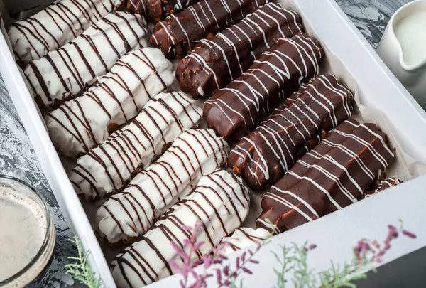 Kutuda beyaz ve çikolata jöleli ekler ya da profiteroller ve gri ahşap arka planda bahar çiçekleriyle kaplı tabağın üzerinde. Tatlılar, tatlı ve pasta, üst manzara, kapat.