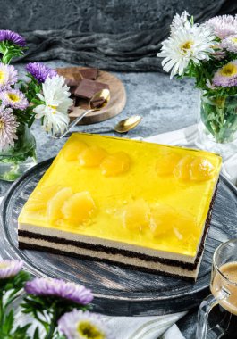 Gri arka planda ananas jöleli sarı kremalı kek, bir fincan kahve, çikolata ve çiçekler. Tatlılar, tatlı ve pasta, üst manzara