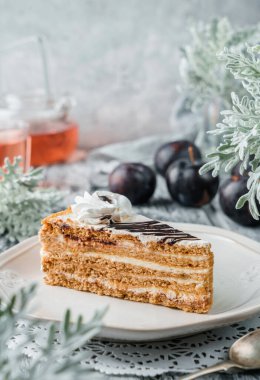 Krema ve reçelli bir dilim lezzetli kek gri arka planda taze erikler, bitkiler ve çiçeklerle birlikte. Tatlılar, tatlı ve pasta, yakın çekim, seçici odaklanma