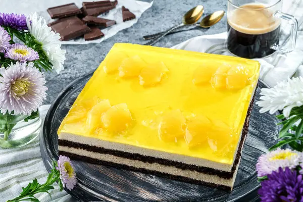 Yellow mousse cake with pineapple jelly on grey background with cup of coffee, chocolate and flowers. Sweets, dessert and pastry, top view