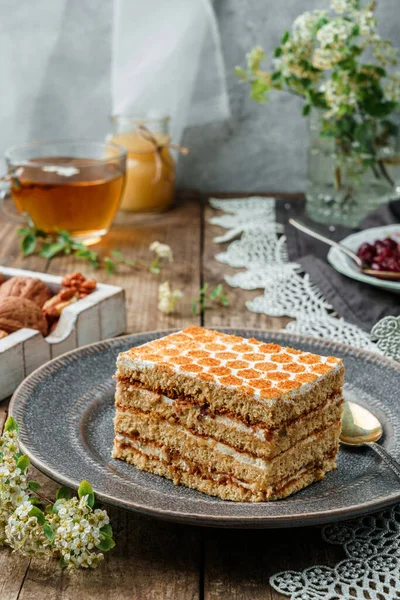 Piece of delicious honey cake with walnuts and honey on wooden background with cup of tea and spring flowers. Sweets, dessert and pastry, homemade cakes, close up, selective focus