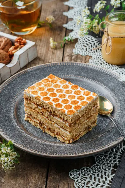 Piece of delicious honey cake with walnuts and honey on wooden background with cup of tea and spring flowers. Sweets, dessert and pastry, homemade cakes, top view, selective focus