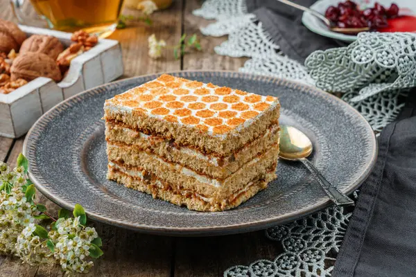 Piece of delicious honey cake with walnuts and honey on wooden background with cup of tea and spring flowers. Sweets, dessert and pastry, homemade cakes, close up, selective focus