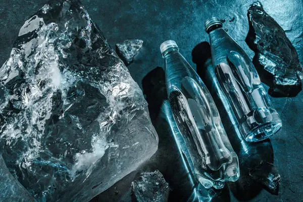 Dvě Láhve Vody Ledu Kamenném Pozadí Kousky Ledu Osvětlené Modrým — Stock fotografie