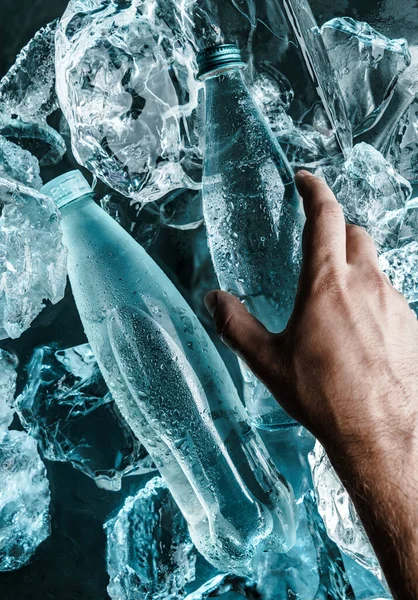 男は氷に水のボトルを持っている ブルーライトで照らされた氷の部分 ガラス ビンの広告のミネラル ウォーター 上の眺め — ストック写真