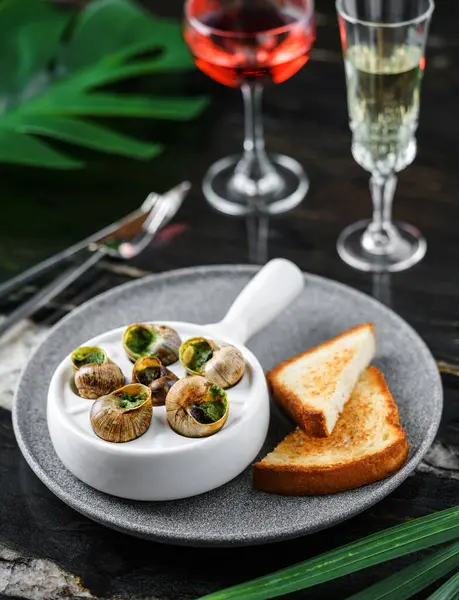 Delicious sea snails with herbs and bread on plate over marble background with drinks. Gourmet food. Escargot Snails, top view