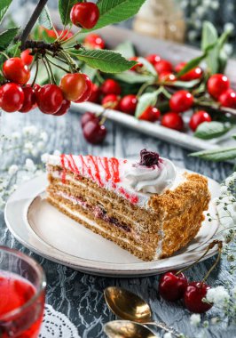 Kremalı ve reçelli bir dilim lezzetli kek, kirazlı tabakta, gri arka planda, dalda taze kirazlar var. Tatlılar, tatlı ve pasta, yakın çekim, seçici odaklanma