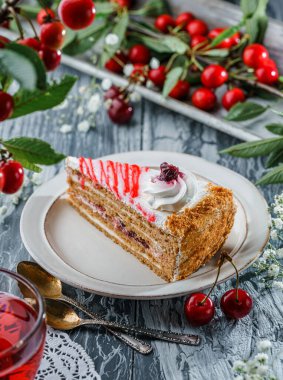 Kremalı ve reçelli bir dilim lezzetli kek, kirazlı tabakta, gri arka planda, dalda taze kirazlar var. Tatlılar, tatlı ve pasta, üst görünüm, seçici odaklanma