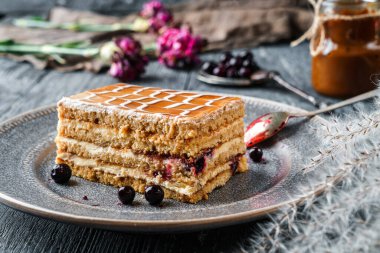 Lezzetli ballı bisküvi keki, böğürtlenli ve yoğunlaştırılmış sütle dolu gri ahşap arka planda böğürtlen ve çiçeklerle kaplı. Tatlılar, tatlı ve pasta, üst görünüm, seçici odaklanma