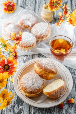 Vanilyalı, kremalı, pudra şekerli, ahşap zemin üzerinde çay ve çiçeklerle birlikte nefis kek donutları. Tatlılar, tatlı ve pasta, yaklaşın.