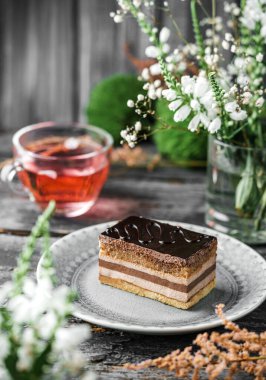 Çikolata jöleli bir parça lezzetli sufle kek, ahşap zemin üzerinde krema, çiçekler ve bir fincan çay. Tatlılar, tatlı ve pasta, yaklaşın.