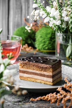 Çikolata jöleli bir parça lezzetli sufle kek, ahşap zemin üzerinde krema, çiçekler ve bir fincan çay. Tatlılar, tatlı ve pasta, yaklaşın.