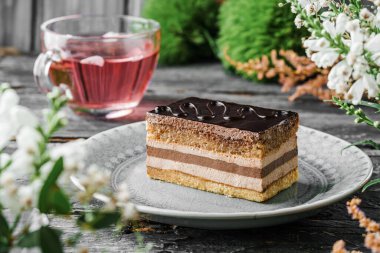 Çikolata jöleli bir parça lezzetli sufle kek, ahşap zemin üzerinde krema, çiçekler ve bir fincan çay. Tatlılar, tatlı ve pasta, yaklaşın.