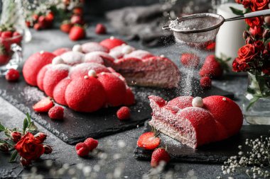 Sütlü, çilekli ve şekerli kırmızı süt kremalı kek ve koyu taşlı arka planda süt, çilek ve çiçeklerle. Tatlılar, tatlı ve pasta, yaklaşın.