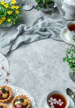 Yemek pişirmek ya da yemek pişirmek. Açık gri arka planda peçete, çiçek, mini sepet kek ya da turta keki, bir fincan çay. Üst görünüm, kopyalama alanı, metin alanı