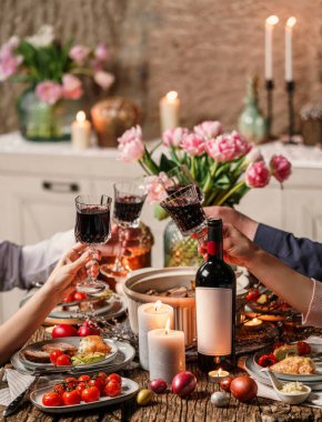 Bir grup mutlu arkadaş şarap bardaklarına yapışıyorlar. Paskalya bayramı masasında şarap, renkli yumurta, sebzeli fırında et, mumlar, evde şenlikli bir akşam yemeği için çiçekler. Kutlama konsepti, tonlama