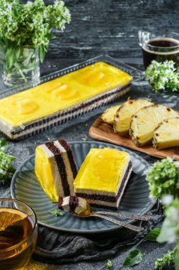 Ananas jöleli sarı kremalı pasta ve bir fincan çay, meyve ve çiçeklerle taş zemin üzerinde çikolata. Tatlılar, tatlı ve pasta, üst manzara