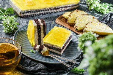 Ananas jöleli sarı kremalı pasta ve bir fincan çay, meyve ve çiçeklerle taş zemin üzerinde çikolata. Tatlılar, tatlı ve pasta, üst manzara