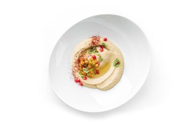 Tabakta kremalı humus, nohut, nar tohumu ve beyaz arka planda izole edilmiş taze otlarla süslenmiş. Sağlıklı yiyecekler, vejetaryen diyeti, yakın çekim, üst manzara.