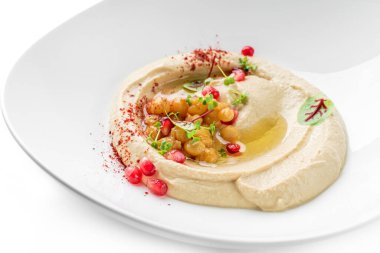 Tabakta kremalı humus, nohut, nar tohumu ve beyaz arka planda izole edilmiş taze otlarla süslenmiş. Sağlıklı yiyecekler, vejetaryen diyeti, yakın çekim, üst manzara.