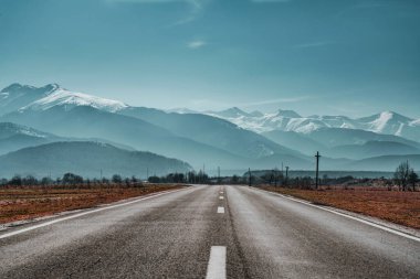 Dağlara giden boş asfalt yol. Dağlık arazideki otoyol manzarası güneş ışınlarıyla dolu. Dağ yolu manzaralı güzel doğa gezisi