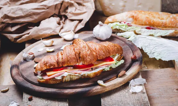 Çıtır çıtır ve lezzetli Fransız kruvasan sandviçi jambon, pastırma, peynir, marul, ahşap kesim tahtasında domatesler. Et, kahvaltı, hamur işi, yakın çekim.