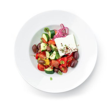 Domatesli, soğanlı, dolmalık biberli, salatalıklı, zeytinli, beyaz arkaplanlı taze sebzeli Yunan salatası. Sağlıklı yiyecekler, vejetaryen diyeti, üst manzara, yakın çekim.