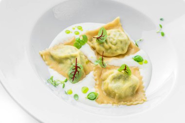 Beyaz arka planda, ıspanaklı Ravioli ve ekşi kremalı ricotta peyniri. Vejetaryen yemekleri, üst manzara, yakın çekim.