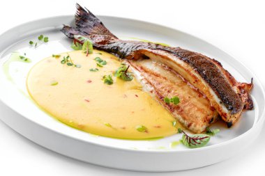 Soslu ızgara fileto Dorado balığı ve beyaz arka planda izole edilmiş tabakta yeşillikler. Sağlıklı deniz ürünleri, üst manzara, yakın çekim.