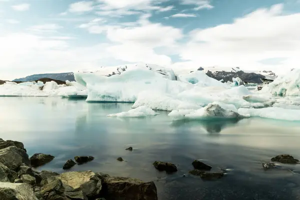 冰原冰川湾的景观 白色的小冰块流过水面 岩石海岸在前景中 冰河与天空 背景为白云 — 图库照片#