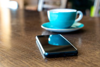 Akıllı telefon ve turkuaz bardak gündelik ortamda ahşap masanın üzerinde.