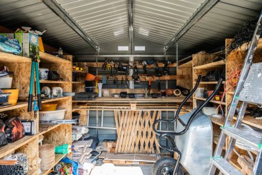 Işıl ışıl bir atölye ortamında inşa ve bahçe aletleri içeren organize raflarla dolu araç deposunun iç görünümü