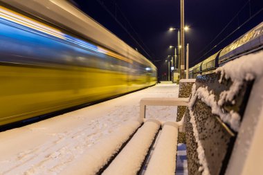 Sarı tren gece Polonya 'da karlı istasyonda hızla ilerliyor. Hareket bulanıklığı, ulaşım ve kış yolculukları için ideal.