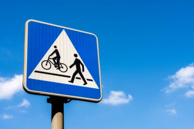 Mavi gökyüzü arkaplanından geçen yaya ve bisikletçi için Polonyalı trafik işareti, yol güvenliğini ve paylaşılan yolu simgeliyor
