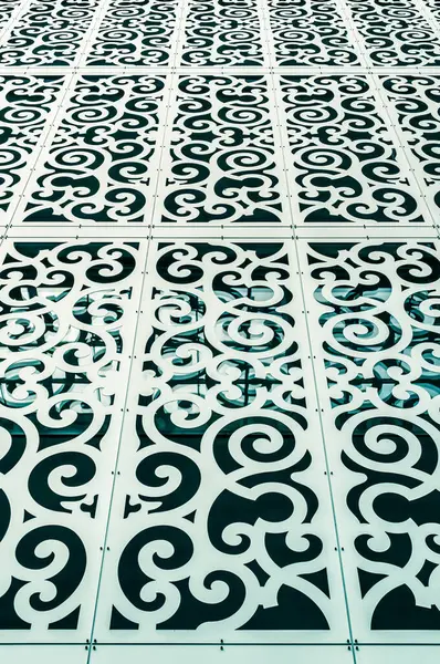Perspektif görünümünde dönen geometrik motifler içeren dekoratif delikli metal paneller ile modern mimari cephe