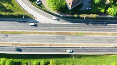 Bahar güneşinde üst geçitlerle ve arabalarla çoklu şeritli yol kesişiminin yukarıdan aşağı hava görüntüsü, kentsel trafik akışı