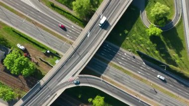 Çok şeritli yol ve kıvrımlı üst geçitin yeşil kentsel çevrede kesişen demiryolu hattının tepeden aşağı dönen görüntüsü