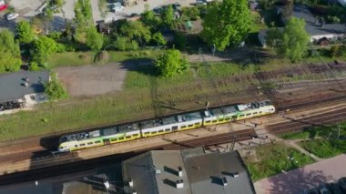 Baharda küçük tren istasyonundan kalkan yeşil-sarı modern yolcu treninin havadan görünüşü, ulaşım ve seyahat teması