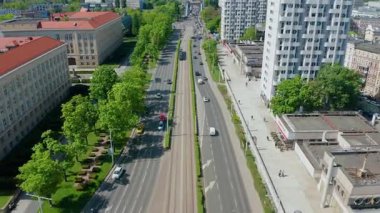 Gün ışığında yeşil ağaçlar ve modern binalarla bölünmüş bulvar boyunca giden tramvay manzarası