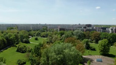 Güneşli bahar günlerinde sık ağaçlar ve modern apartman blokları olan şehir parkının panoramik drone görüntüsü.