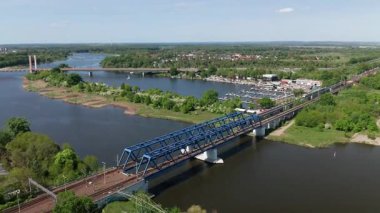 Nehrin üzerindeki çelik demiryolu köprüsünün havadan görüntüsü. Yolcu treni geçiyor. Yeşillik yemyeşil, ulaşım altyapısı