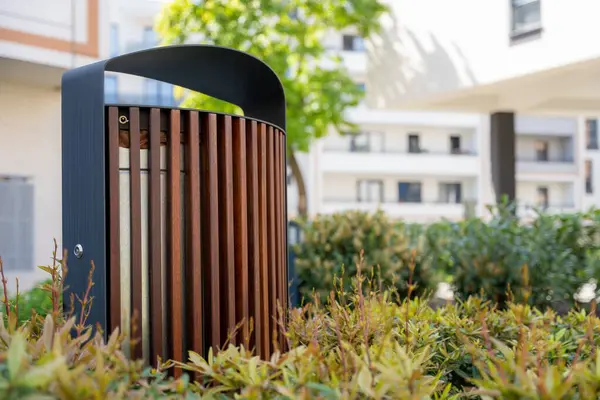 Dikey tahta levhalarla modern çöp tenekesi ve konut avlusunda çalılar ve binalarla birlikte metal kaplanmış, kentsel tasarım detaylarına odaklanmış.
