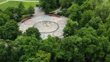 Polonya 'daki dekoratif bir çeşme plazasının yüksek görünümü eşmerkezli daire desenleri içeriyor ve yemyeşil, gösterişli kentsel manzara tasarımı ve açık hava eğlencesi ile sınırlandırılıyor.